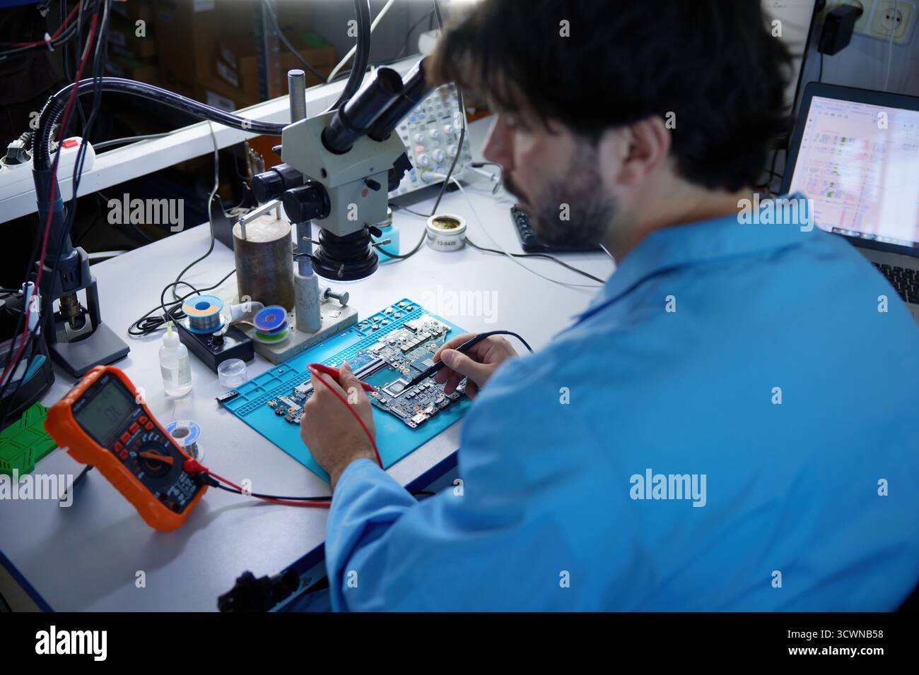 Il tecnico si è impegnato attivamente in lavori critici sulla scheda a circuiti stampati osservando al microscopio Foto Stock