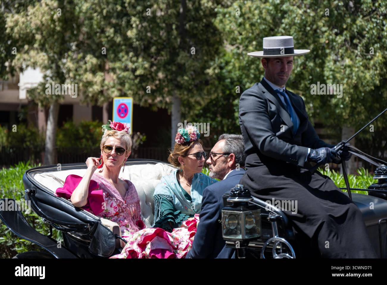 Siviglia, Spagna - 23 apr 23: Un'elegante carrozza trainata da cavalli con persone elegantemente vestite, con un uomo in abbigliamento formale alla guida e due donne in c Foto Stock