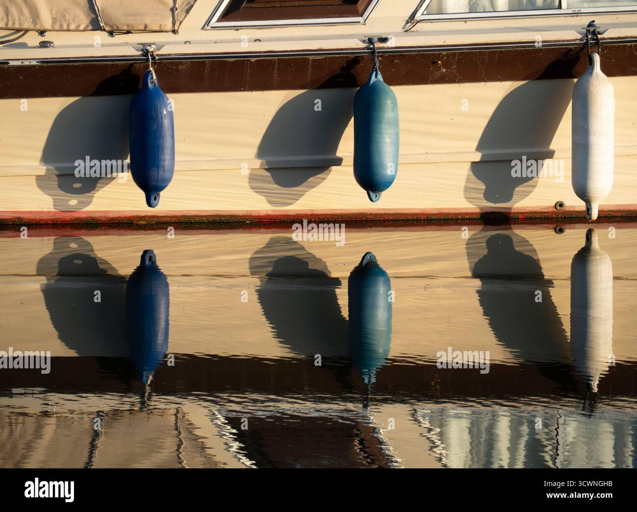 Barca da diporto ormeggiata sul Tamigi ad Abingdon, con boe sospese. È interessante notare che questi dispositivi anticollisione/ancoraggio riempiti di schiuma sembrano avere molti nomi, variamente - parafanghi, boe per imbarcazioni, paraurti, parafanghi con boa... scegliete voi. Ma qui le boe e i loro riflessi nel fiume rendono un'interessante composizione astratta... Foto Stock