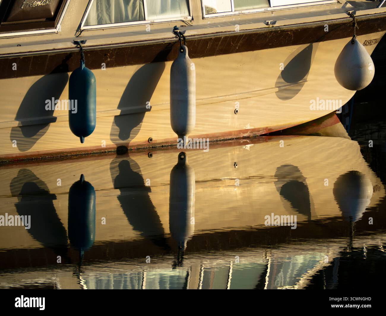 Barca da diporto ormeggiata sul Tamigi ad Abingdon, con boe sospese. È interessante notare che questi dispositivi anticollisione/ancoraggio riempiti di schiuma sembrano avere molti nomi, variamente - parafanghi, boe per imbarcazioni, paraurti, parafanghi con boa... scegliete voi. Ma qui le boe e i loro riflessi nel fiume rendono un'interessante composizione astratta... Foto Stock