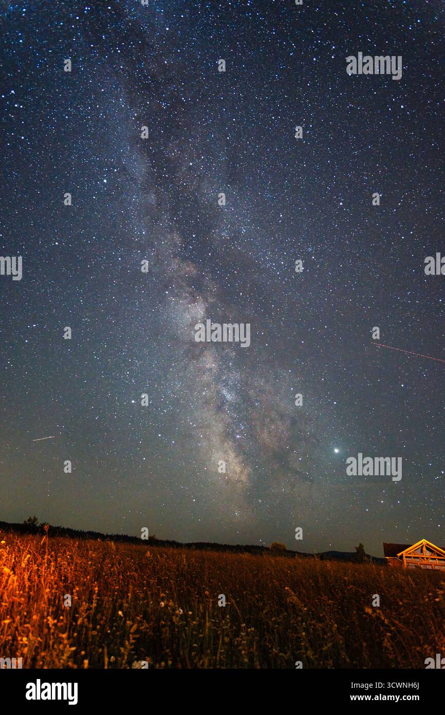 Via Lattea sul campo di campagna con orizzonte luminoso e piccola casa Foto Stock