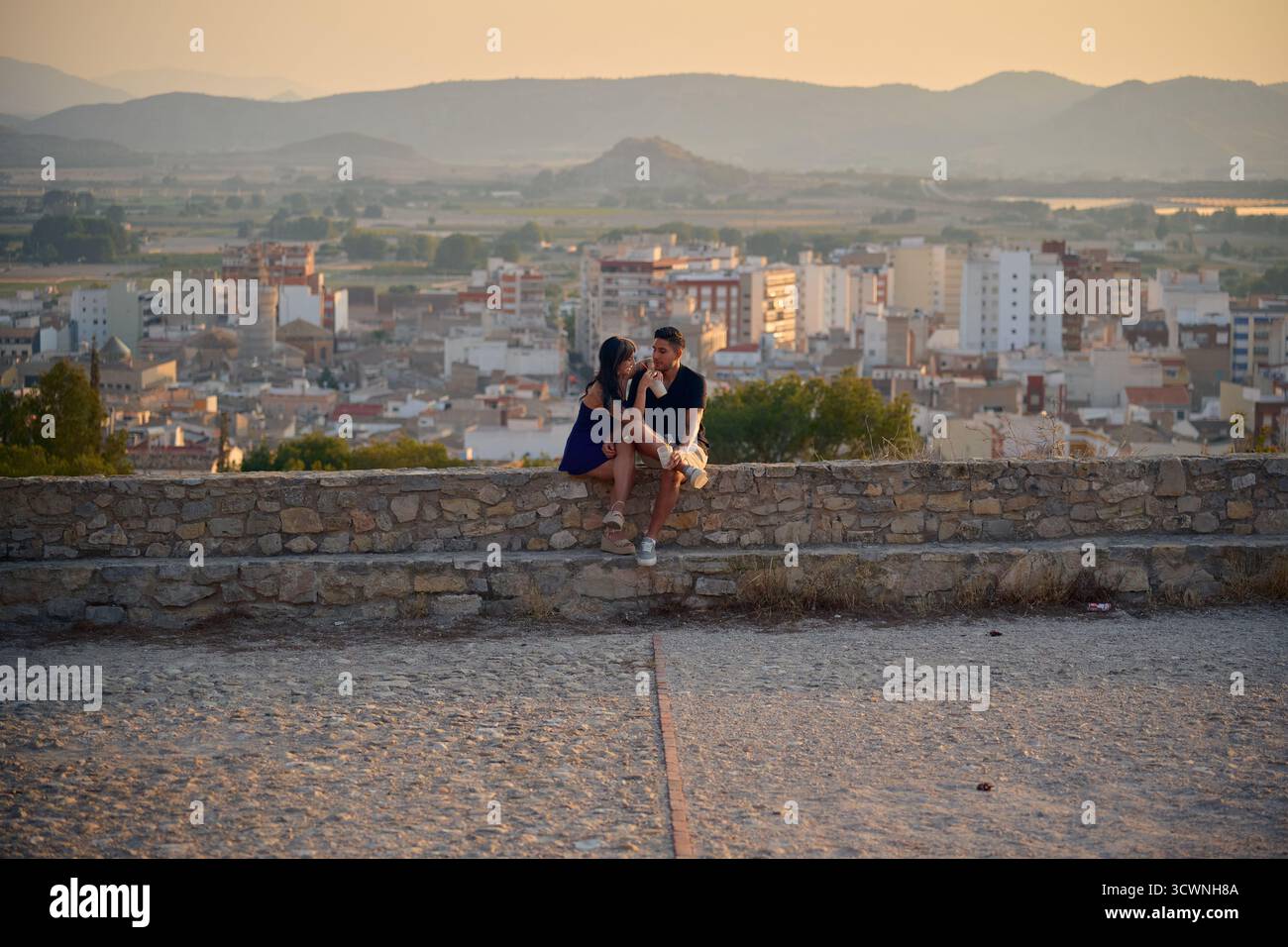 Giovane coppia che mostra romanticismo seduto su un muro con vista sulla città Foto Stock