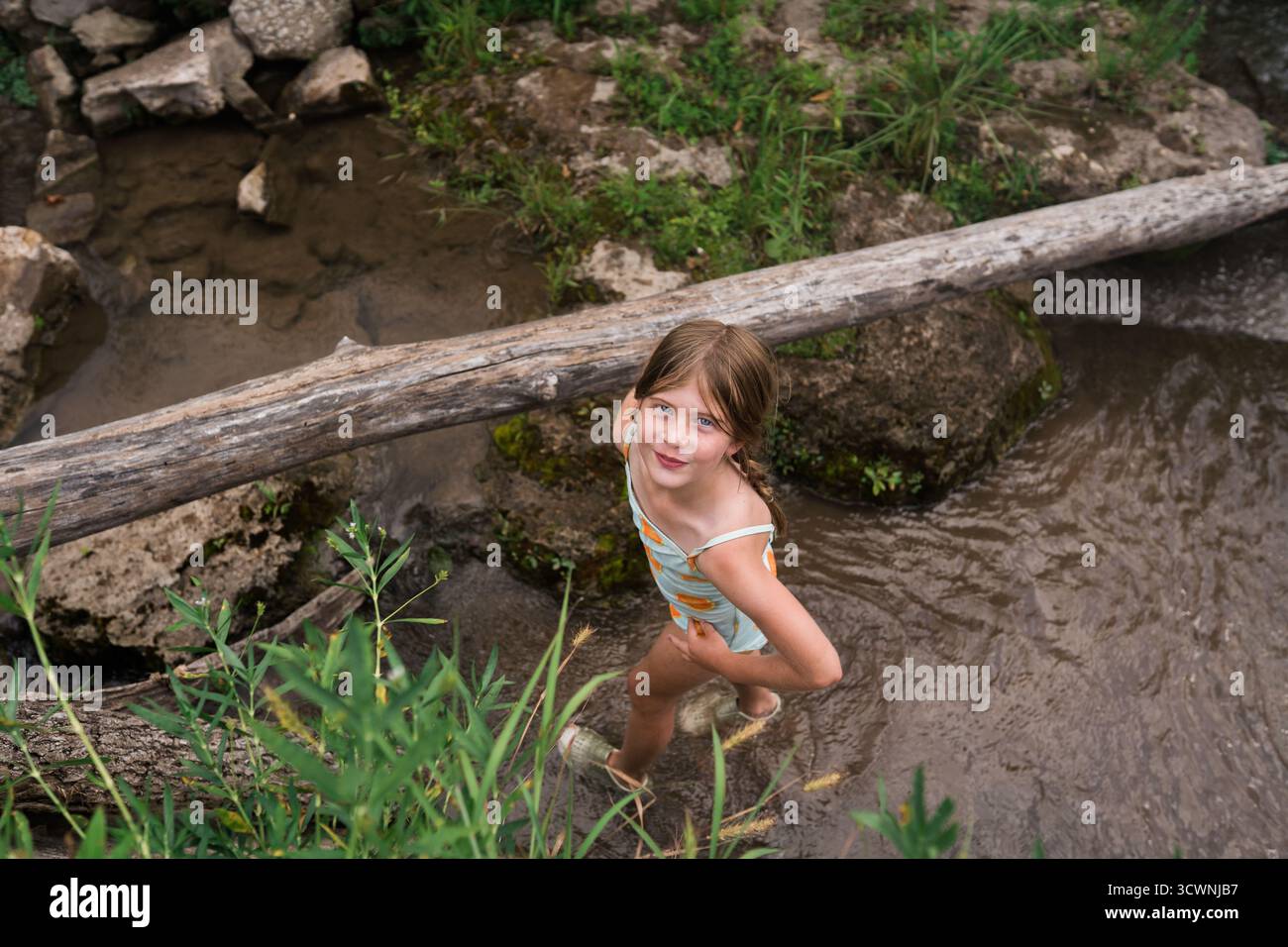 Ragazza sorridente in costume da bagno in piedi in basso torrente vicino al tronco caduto. Foto Stock