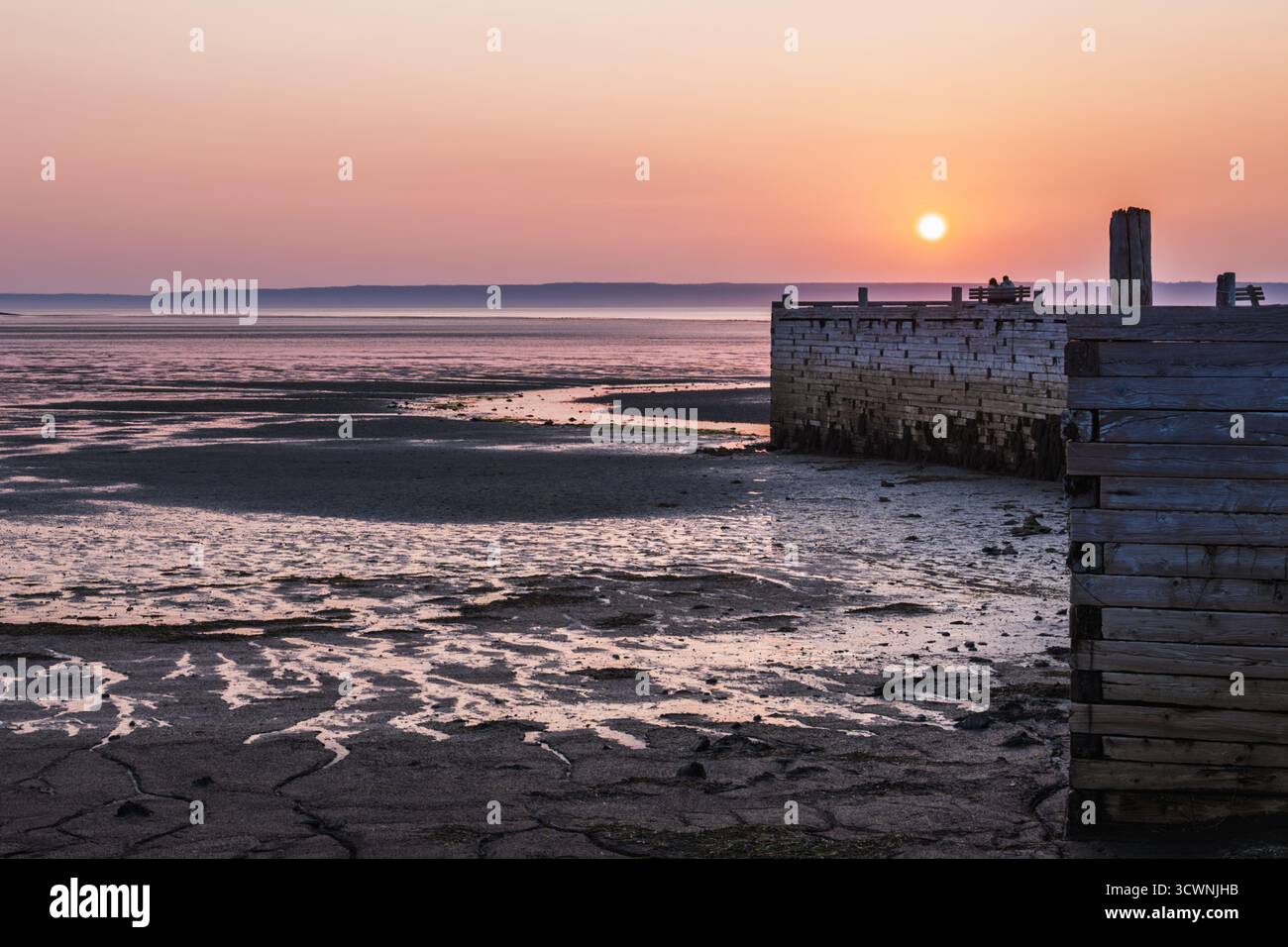 Il tramonto sulla bassa marea al molo costiero è piacevole per la coppia sulla panchina da picnic Foto Stock