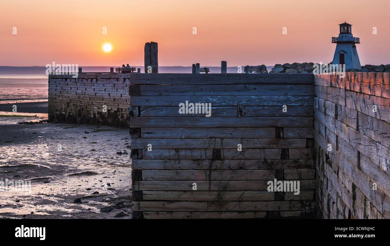 Coppia che guarda il tramonto sul molo di legno con il faro Foto Stock