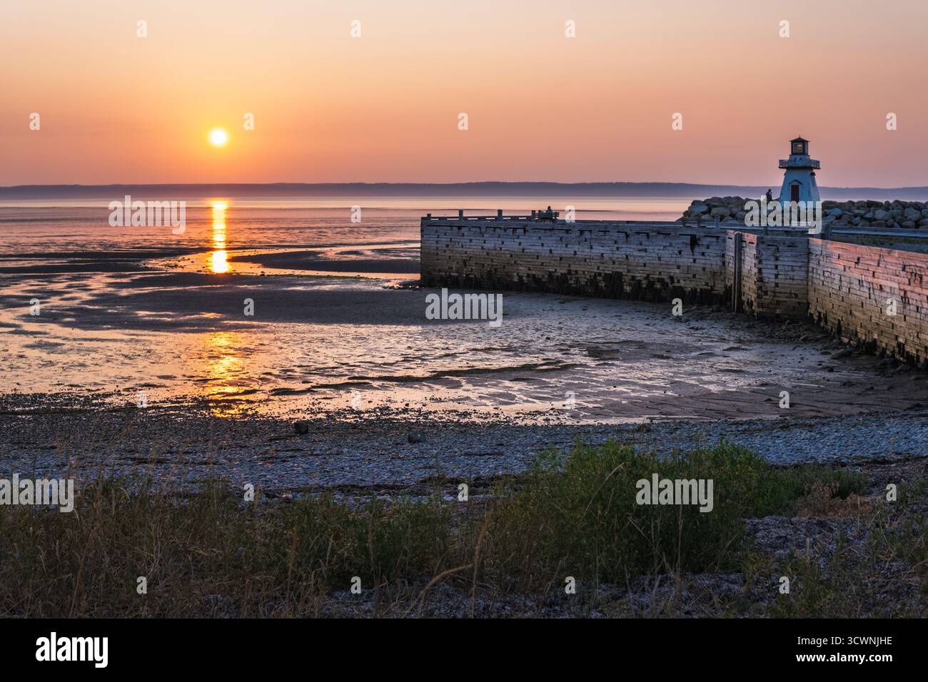 Faro e tramonto che si riflettono sulle piane mareali Foto Stock