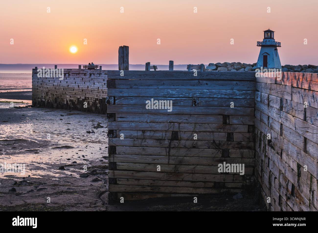 La coppia gode di momenti di tramonto su un molo di legno con faro Foto Stock