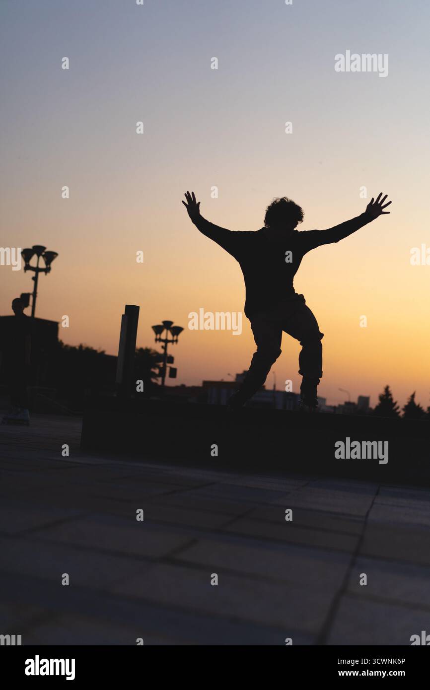 Uomo che esegue un trucco sui pattini al tramonto, in un ambiente urbano Foto Stock