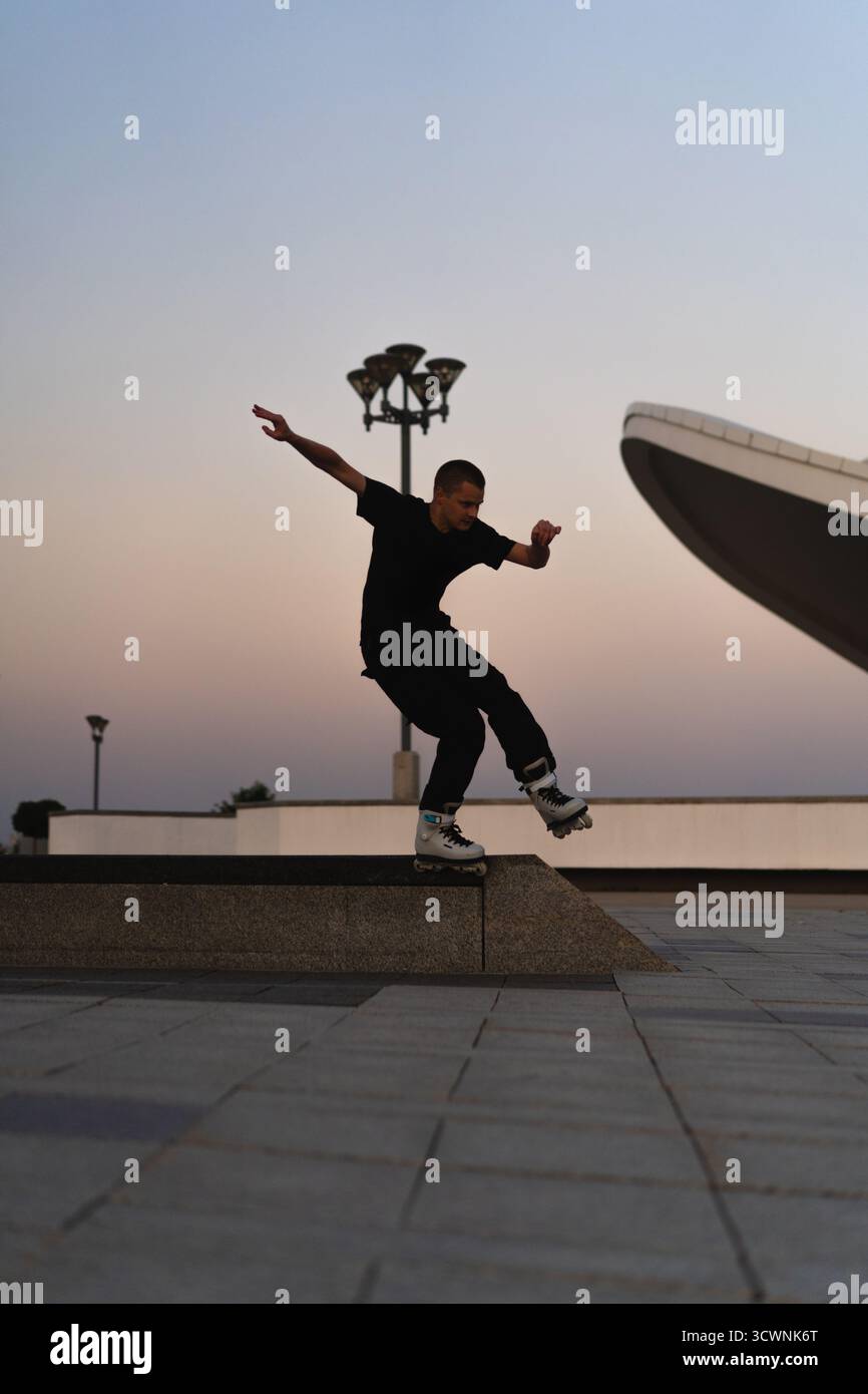 Uomo che esegue un trucco sui pattini al tramonto, in un ambiente urbano Foto Stock