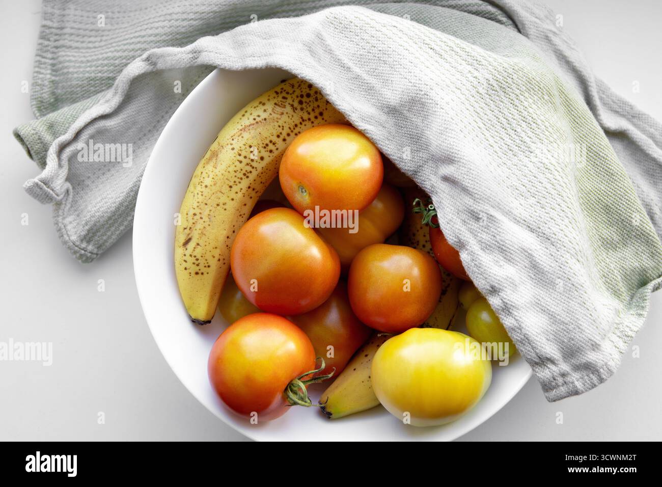 La maturazione di pomodori verdi crudi con banane è efficace perché il gas etilenico della banana accelera il processo. Foto Stock