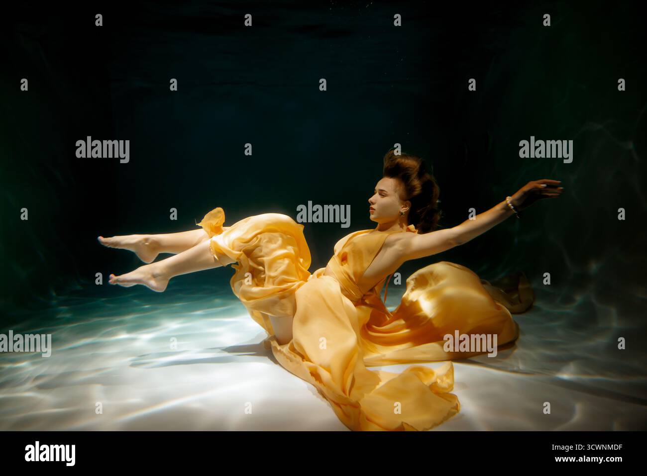 Donna in abito giallo fluente sott'acqua creando una scena serena Foto Stock