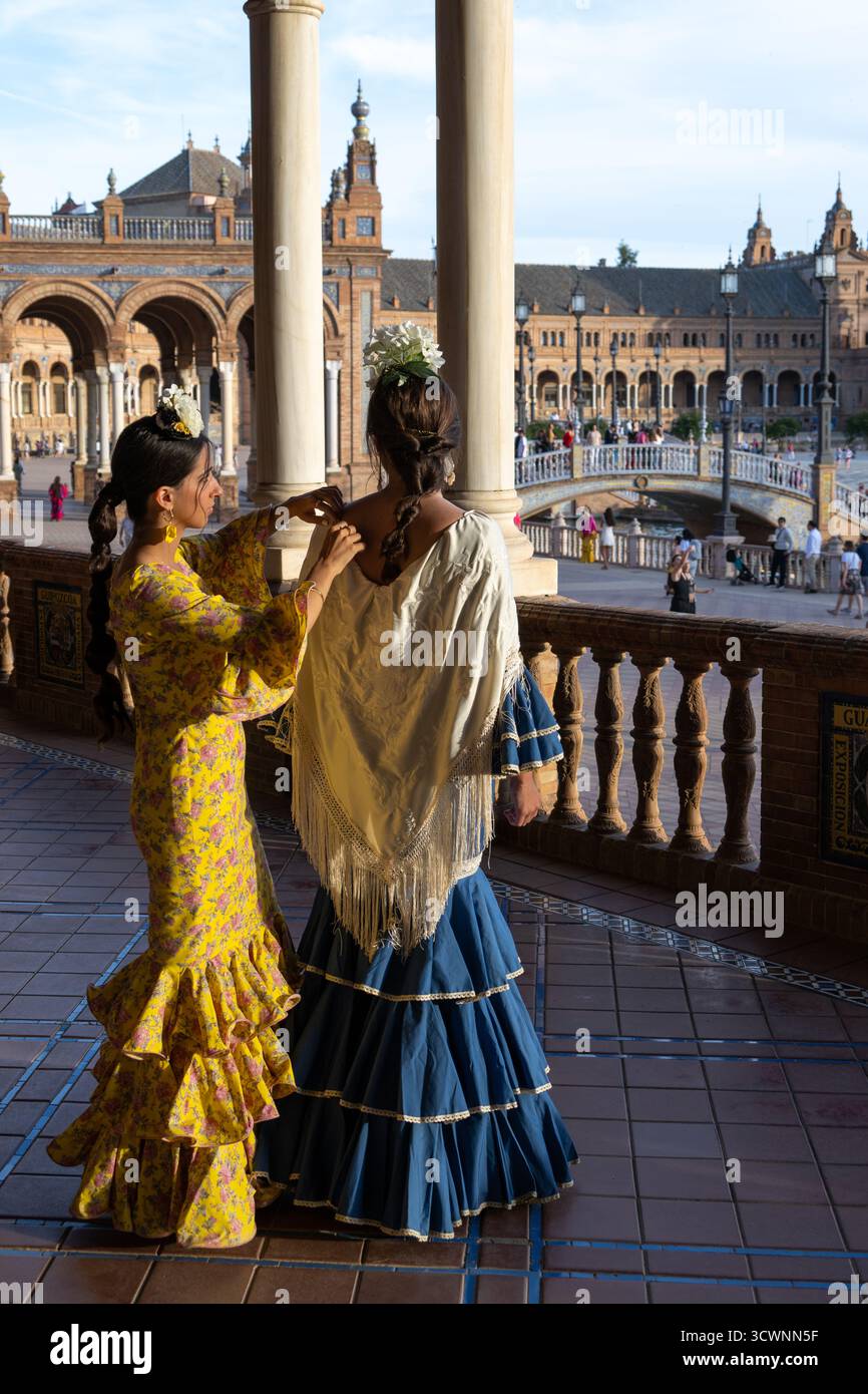 Siviglia, Spagna - 23 apr 23: Due donne in abiti tradizionali spagnoli in una piazza storica, una che regola i capelli dell'altra, con un bel architec Foto Stock
