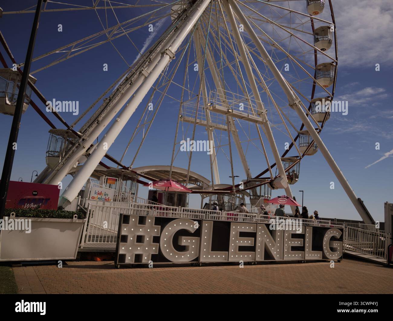 Ruota panoramica gigante e #Glenelg segnano contro un cielo blu profondo. Atmosfera luminosa, soleggiata e gioiosa di un'eccitante giornata estiva al mare. Foto Stock
