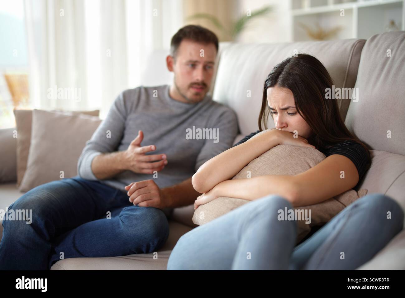 Donna e uomo triste che spiegano seduti su un divano a casa Foto Stock
