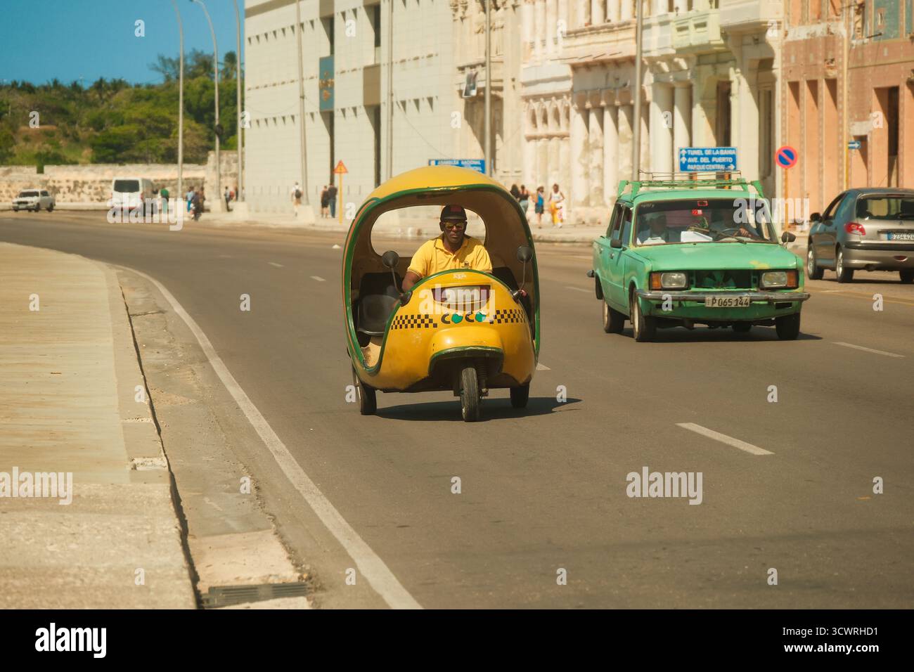 Havana, Cuba 2024 Apr16 - iconico taxi giallo cubano di cocco che guida lungo la strada sul Malecon in una giornata di sole. L'architettura coloniale si affaccia sul lungomare Foto Stock