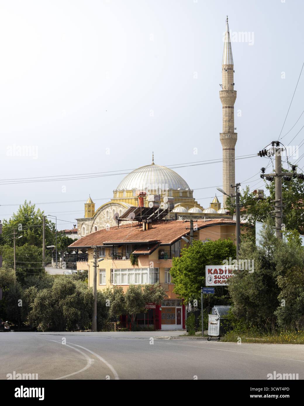 La vista di una moschea con un alto minareto e cupola d'argento si erge maestosamente dietro un edificio accogliente, inondato dalla luce soffusa del giorno, Side, Antalya, Turchia. Foto Stock