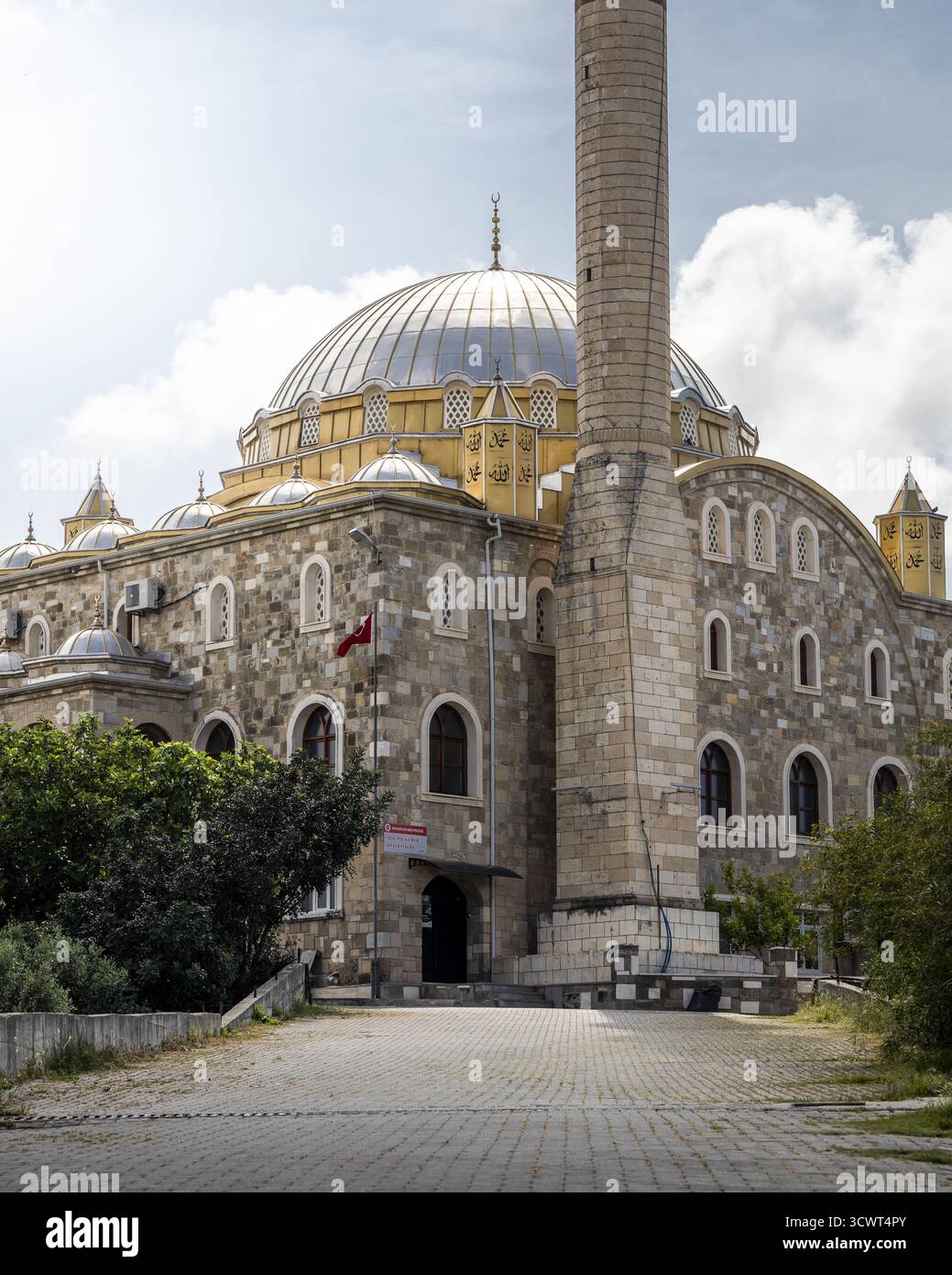Vista di una grande moschea in pietra con una cupola d'argento che splende sotto un cielo nuvoloso, il suo alto minareto che getta un'ombra sul sentiero acciottolato, Side, Antalya, Turchia. Foto Stock