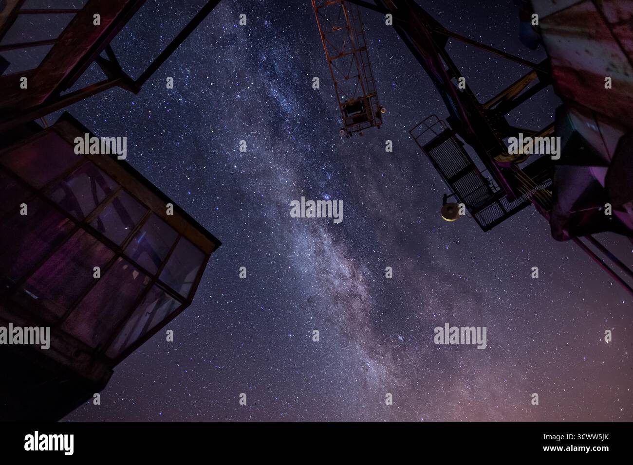 Via Lattea sopra le gru industriali - Fotografia del cielo notturno che mostra la bellezza cosmica e il decadimento urbano con un contrasto incredibile Foto Stock