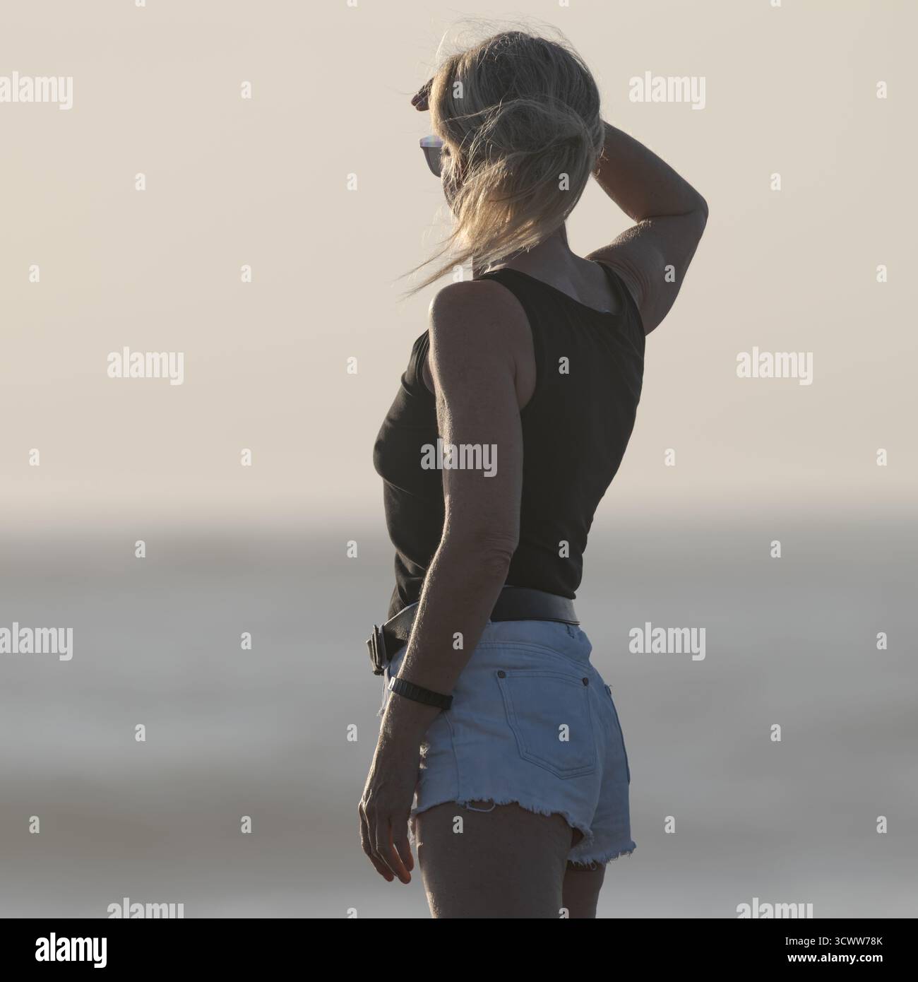 Donna che guarda l'oceano durante il tramonto indossa un casual outfit estivo su una spiaggia tranquilla Foto Stock