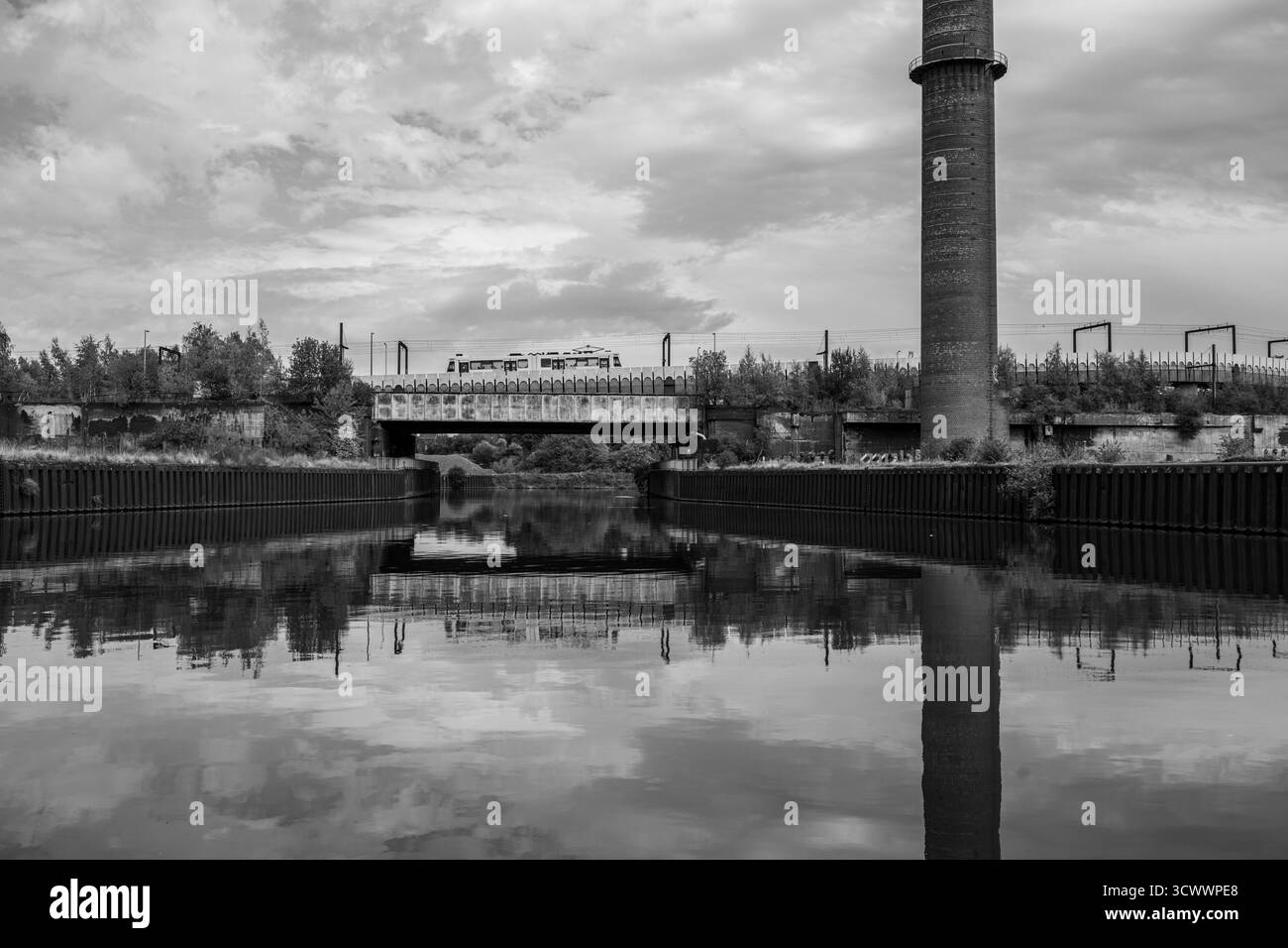 Yellow Train Crossing Industrial Bridge sul Canal con Reflection e Old Chimney - fotografia urbana del paesaggio Foto Stock