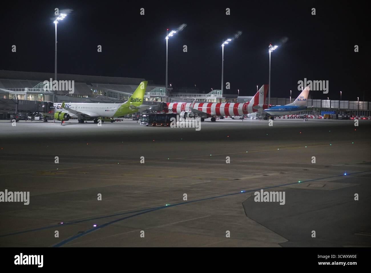 Diversi aerei parcheggiavano sul grembiule dell'aeroporto di Monaco di notte sotto i riflettori luminosi, con veicoli di servizio nelle vicinanze.Monaco, Germania Foto Stock
