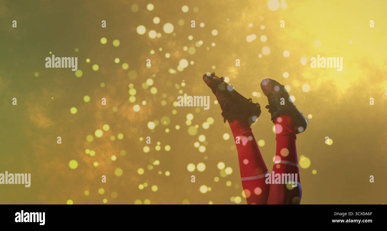 Gambe allungabili con calzini sportivi rossi e scarpe da calcio nere sullo sfondo dorato, spot luminosi Foto Stock