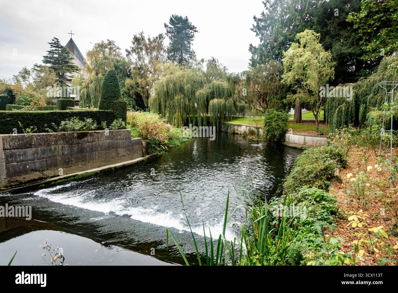 Il fiume Tolka che scorre attraverso Glasnevin, Dublino, Irlanda, con la distesa, giardini all'inglese, alberi e guglie della chiesa visibili sullo sfondo. Foto Stock