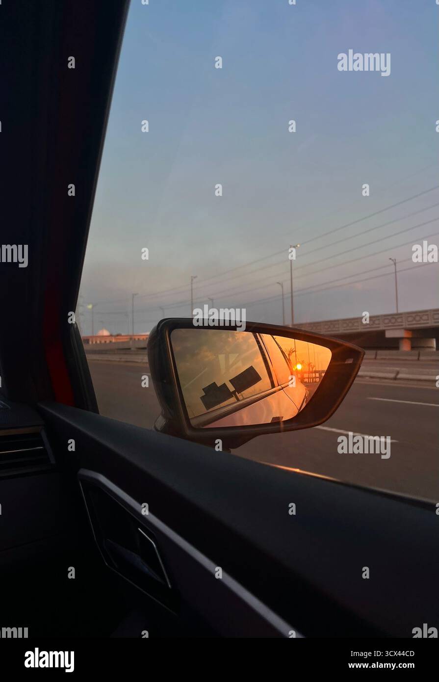 Il tramonto si riflette nello specchio laterale dell'auto durante la guida su un'autostrada tranquilla, catturando un momento di viaggio tranquillo e una calda luce serale. - Immagine stock catturata con smartphone