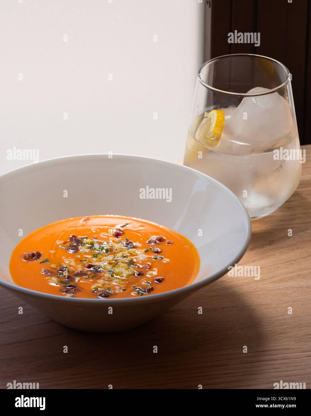 Una ciotola di Salmorejo, una zuppa di pomodoro fredda tipica della Spagna meridionale, su un tavolo con un bicchiere d'acqua con un limone. Foto Stock