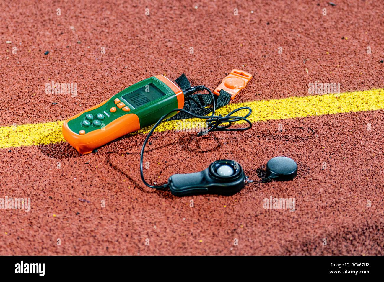 Misuratore di luce digitale arancione, misuratore di lux lumen, su una nuova pista da corsa rossa, utilizzato per misurare l'intensità luminosa in una nuova struttura sportiva all'aperto. Foto Stock