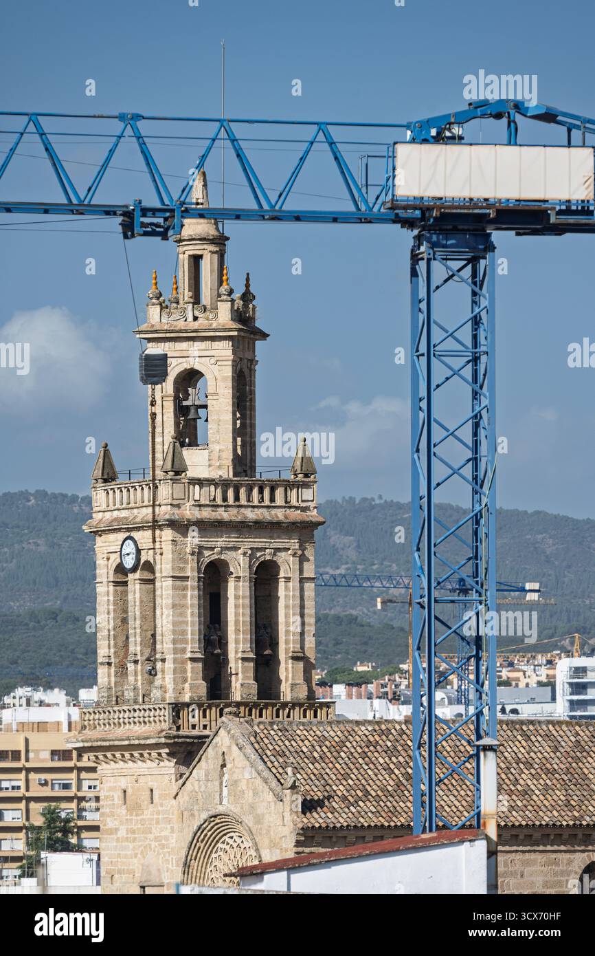 Il campanile di San Lorenzo in Cordoba presenta intricati lavori in muratura e un quadrante dell'orologio, circondato da gru mentre lo sviluppo urbano trasforma il telo Foto Stock
