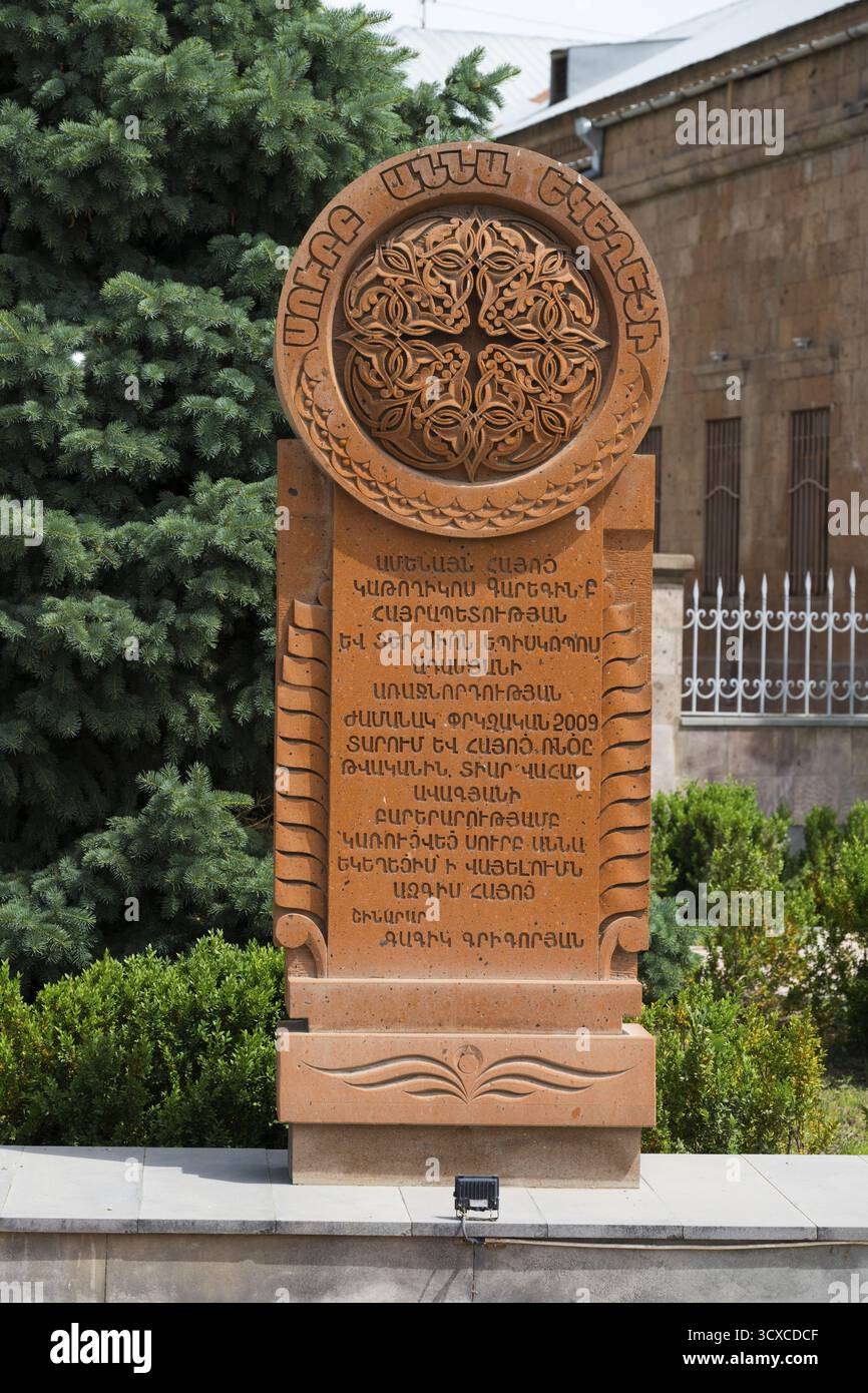 Un khachkar in pietra finemente incisa con ornamenti complessi e caratteri armeni, circondato da alberi e piante, khachkar, pietra a croce, Aghavnat Foto Stock