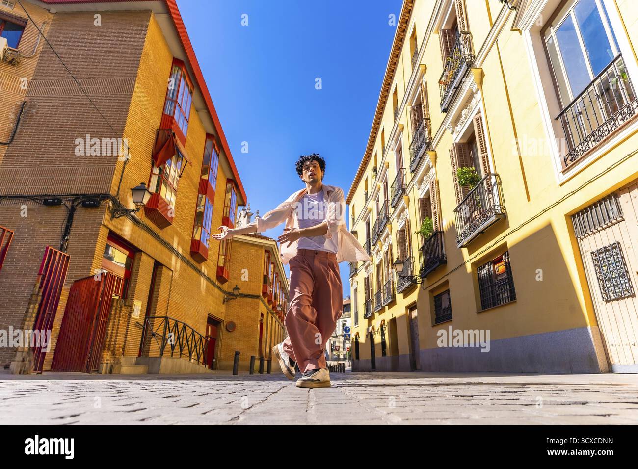 Giovane che danzerà liberamente in una strada acciottolata tra edifici architettonici tradizionali sotto un cielo azzurro, muovendosi con gioia ed esprimendo il suo Foto Stock