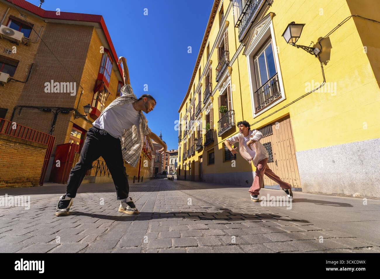Due giovani ballerini maschi che eseguono danza di strada contemporanea si spostano su una soleggiata strada acciottolata, esprimendo il movimento dinamico e la cultura urbana contro di voi Foto Stock