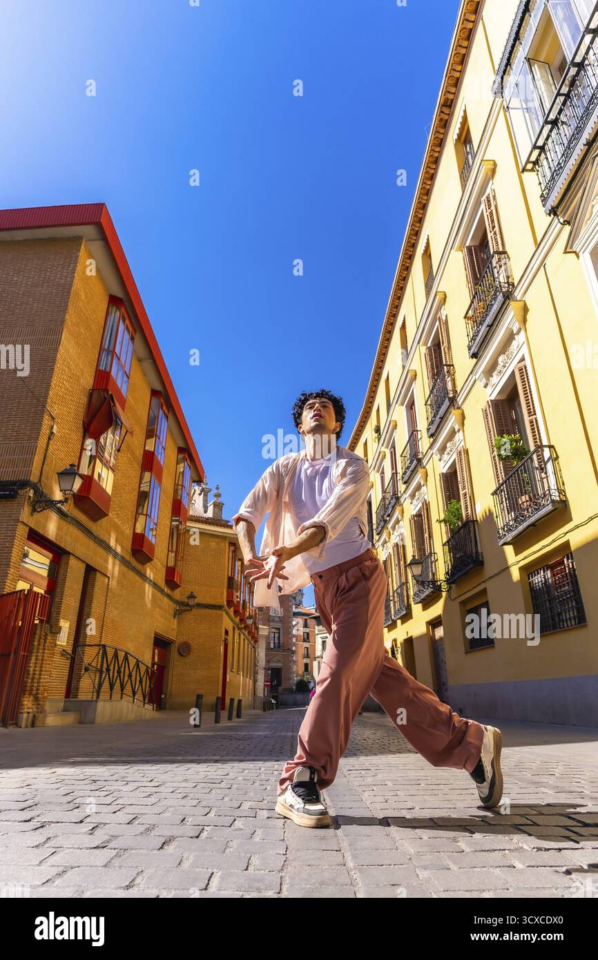 Giovane uomo che esprime movimento e libertà attraverso la danza contemporanea in una vecchia strada europea, creando una scena artistica urbana sotto un chiaro sk blu Foto Stock