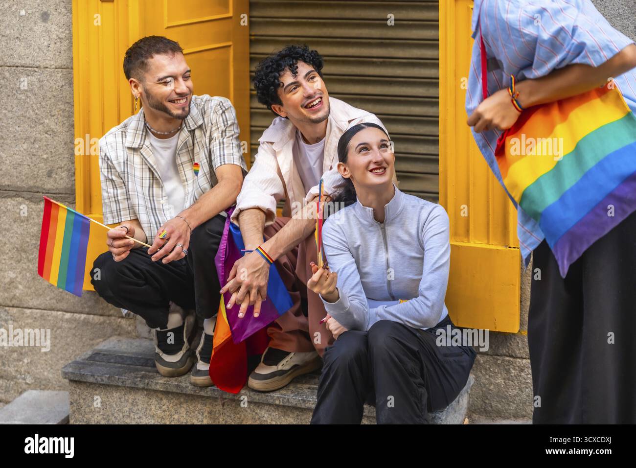 Gruppo di amici diversi che esprimono gioia e appartenenza, tenendo bandiere arcobaleno e portando con sé una borsa arcobaleno, celebrando l'orgoglio gay e lgbtqia e inclusioni Foto Stock