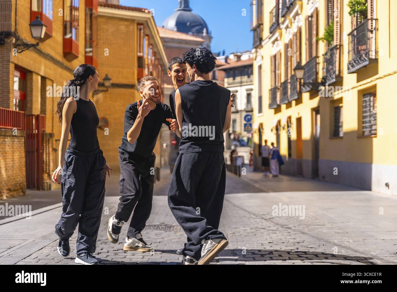 Gruppo di giovani diversi che sorridono, esprimono gioia e libertà mentre eseguono una routine di danza contemporanea all'aperto in un'affascinante strada acciottolata Foto Stock