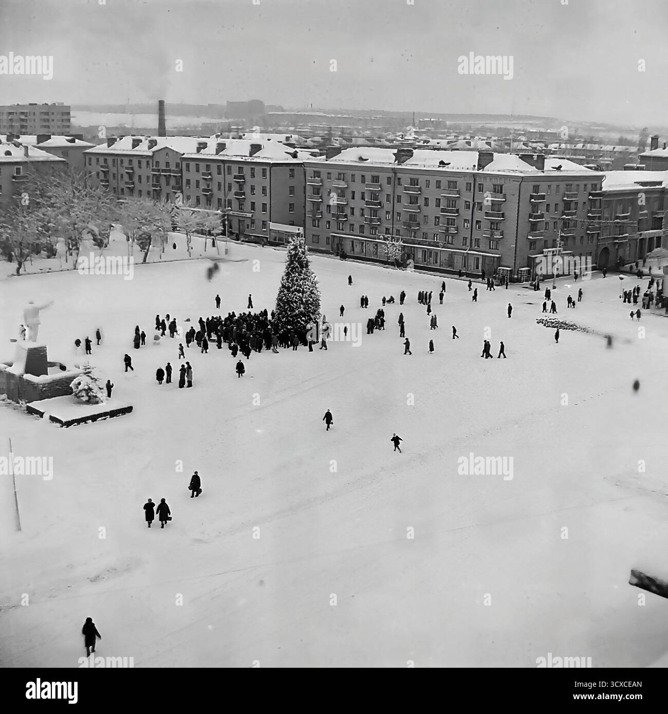 Un'ampia vista d'archivio ad alto angolo dall'inverno 1976 cattura la Piazza della Rivoluzione d'ottobre (ora Piazza Soborna) a Sloviansk, completamente ricoperta di neve. Una folla si raduna intorno all'albero centrale di Capodanno, mentre figure sparse di pedoni attraversano il vasto spazio aperto. Il monumento di Lenin innevato si trova a sinistra, una caratteristica chiave del paesaggio urbano dell'era sovietica. Questa immagine è un record incredibilmente bello del tempo libero invernale e della vita della comunità in un tranquillo Donbas prima della guerra Foto Stock