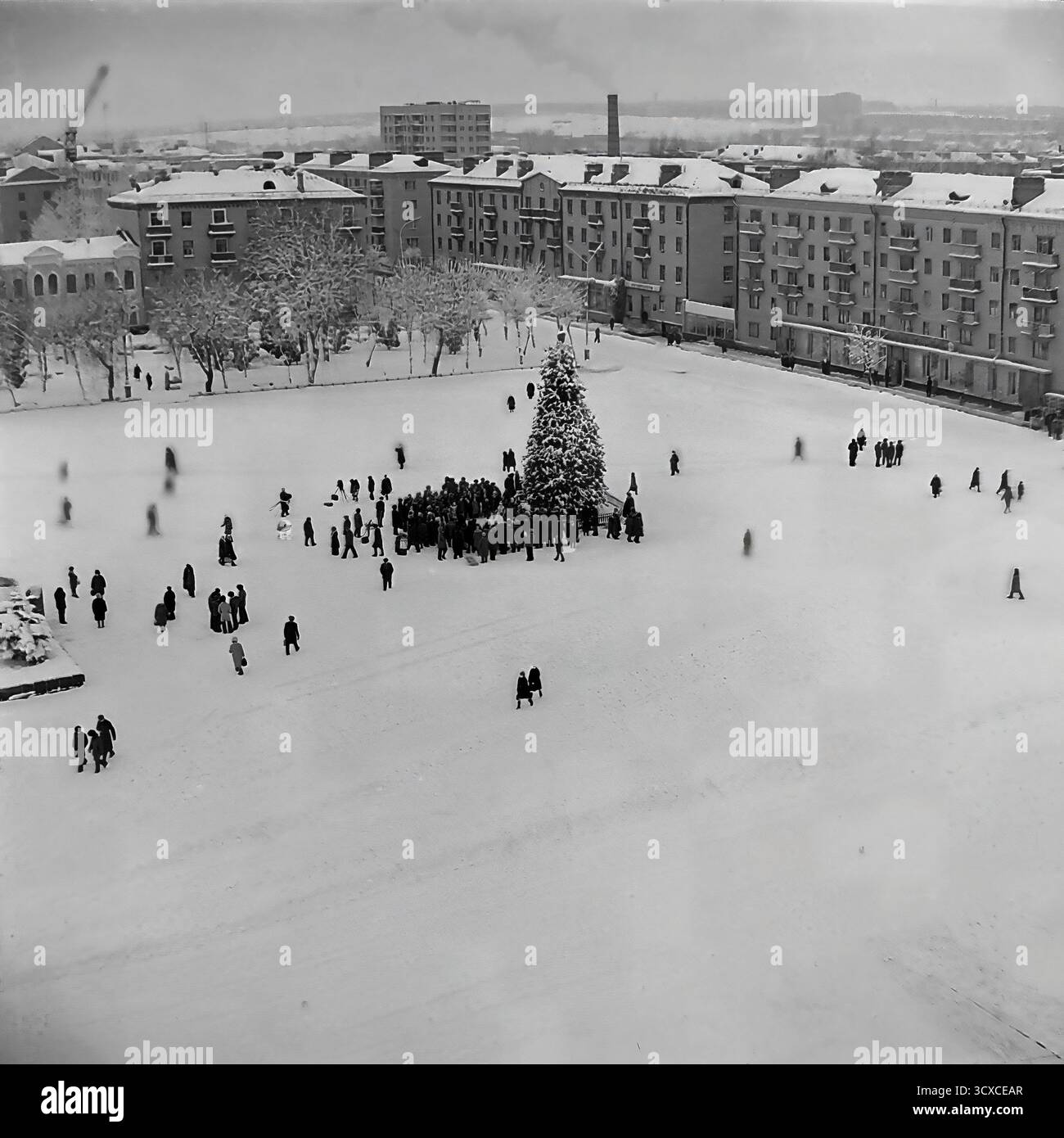 Un'ampia vista d'archivio ad alto angolo dall'inverno 1976 cattura la Piazza della Rivoluzione d'ottobre (ora Piazza Soborna) a Sloviansk, completamente ricoperta di neve. Una folla si raduna intorno all'albero centrale di Capodanno, mentre figure sparse di pedoni attraversano il vasto spazio aperto. Il monumento di Lenin innevato si trova a sinistra, una caratteristica chiave del paesaggio urbano dell'era sovietica. Questa immagine è un record incredibilmente bello del tempo libero invernale e della vita della comunità in un tranquillo Donbas prima della guerra Foto Stock