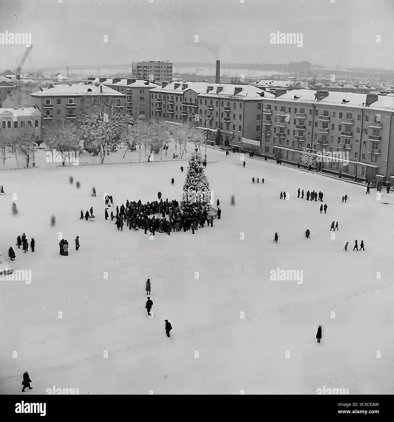 Un'ampia vista d'archivio ad alto angolo dall'inverno 1976 cattura la Piazza della Rivoluzione d'ottobre (ora Piazza Soborna) a Sloviansk, completamente ricoperta di neve. Una folla si raduna intorno all'albero centrale di Capodanno, mentre figure sparse di pedoni attraversano il vasto spazio aperto. Il monumento di Lenin innevato si trova a sinistra, una caratteristica chiave del paesaggio urbano dell'era sovietica. Questa immagine è un record incredibilmente bello del tempo libero invernale e della vita della comunità in un tranquillo Donbas prima della guerra Foto Stock