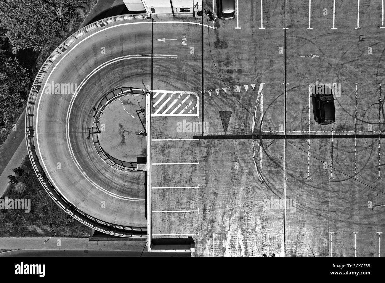 Vista aerea dall'alto verso il basso di un parcheggio a spirale sul tetto con un'auto singola a Rybnik, Polonia, catturata alla luce del giorno con forti ombre e ge Foto Stock