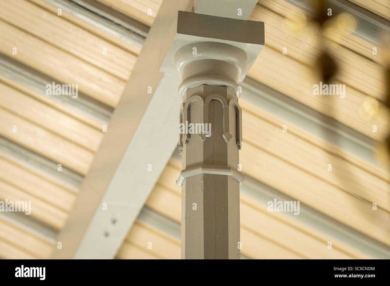 Primo piano di una colonna decorativa in legno con dettagli intagliati e capitello in stile classico, parte di una struttura architettonica interna con luce soffusa. Foto Stock