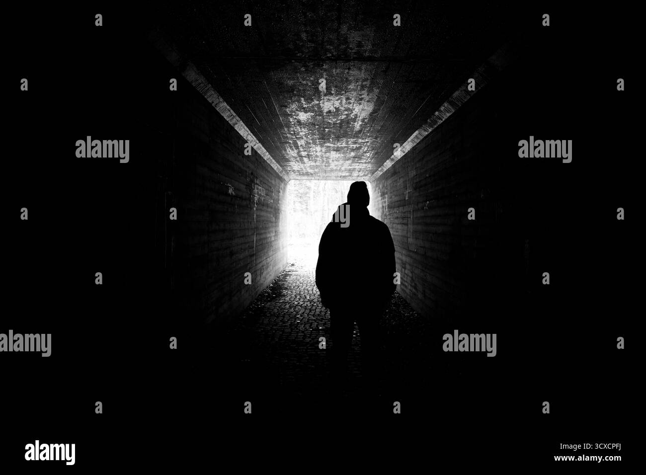 Scena sinistra di uomo in silhouette in un tunnel buio che guarda verso la luce. Scena spaventosa, sfondo scuro e inquietante Foto Stock