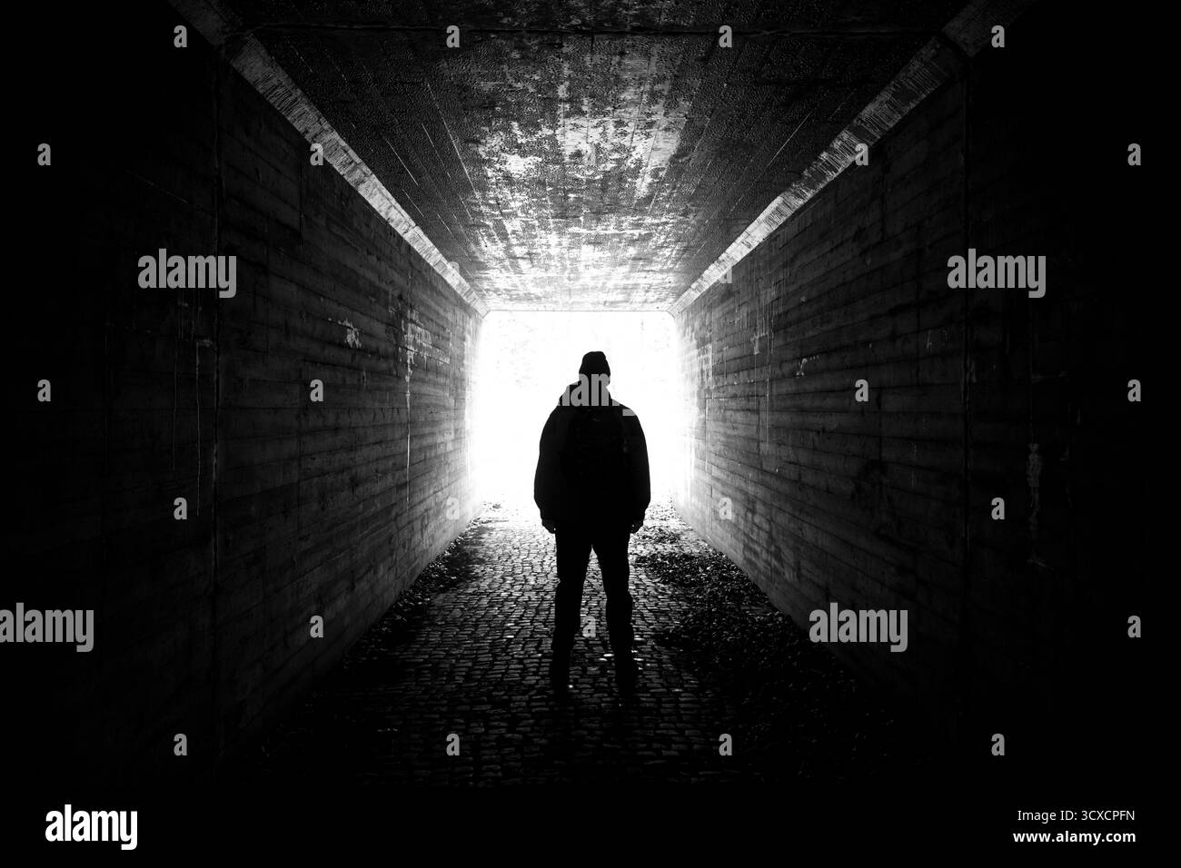 Scena sinistra di uomo in silhouette in un tunnel buio che guarda verso la luce. Scena spaventosa, sfondo scuro e inquietante Foto Stock