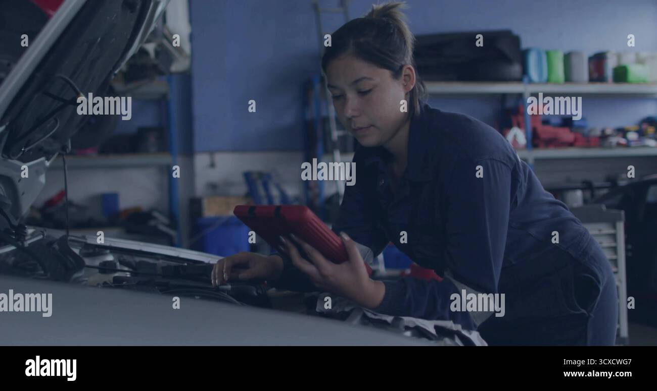 Controllo del motore sotto il cofano aperto in garage, meccanico in tute che tiene una tavoletta rossa su scaffalature Foto Stock