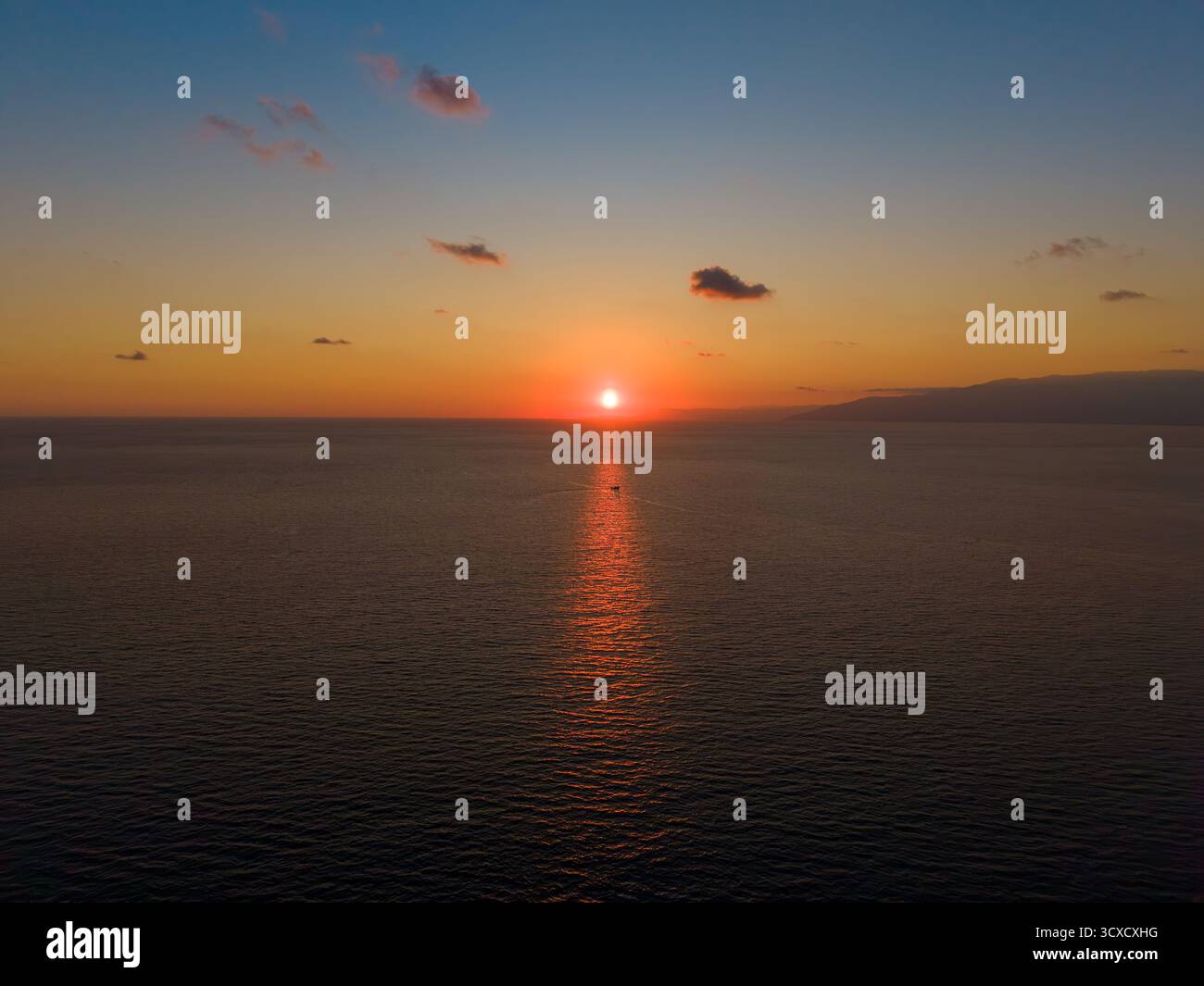 Tramonto dorato che si riflette sul mare con una piccola barca riflessa Foto Stock