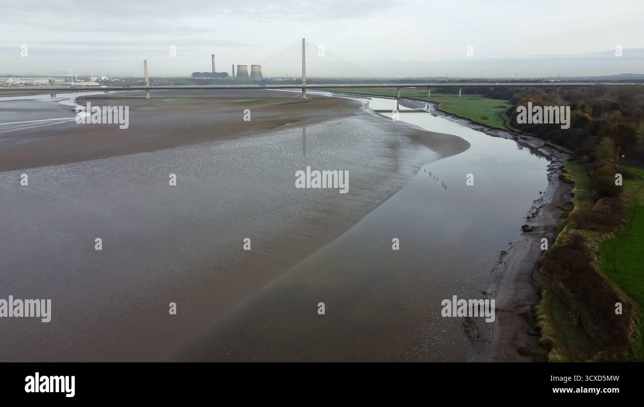 Veduta aerea del Mersey Gateway Bridge che attraversa il fiume Mersey con la bassa marea, con le distese fangose circostanti e le torri di raffreddamento del traghetto Fiddler's Ferry in lontananza Foto Stock