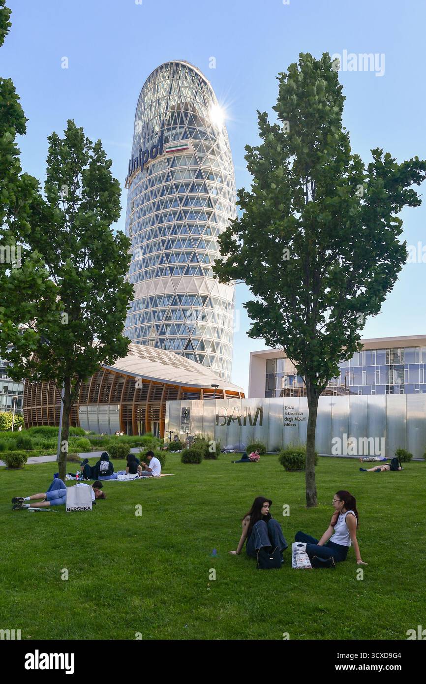 Persone che riposano sul prato del parco pubblico della Biblioteca degli alberi, con gli edifici IBM Studios e Unipol Tower nel centro direzionale di Milano Foto Stock