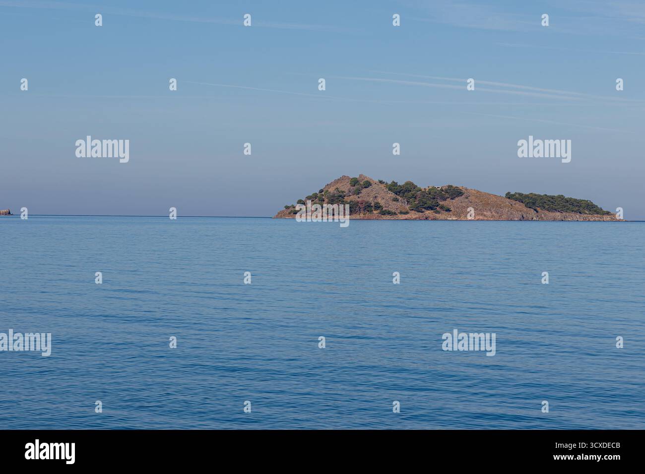 Un'isola tranquilla con vegetazione sparsa circondata da un mare blu calmo sotto un cielo limpido. Foto Stock