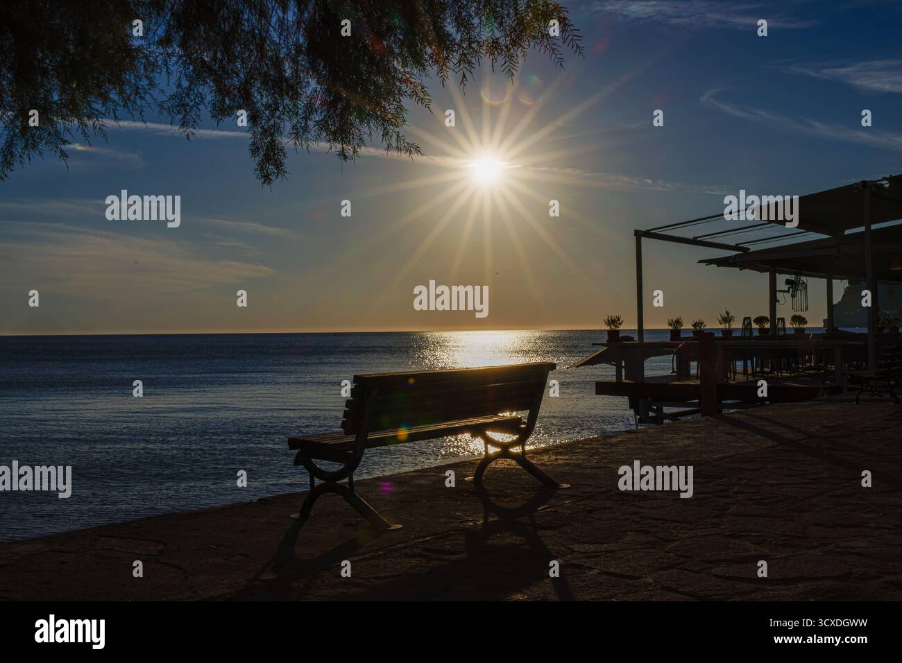 Una tranquilla vista sul mare al tramonto con una panchina e un molo. Foto Stock